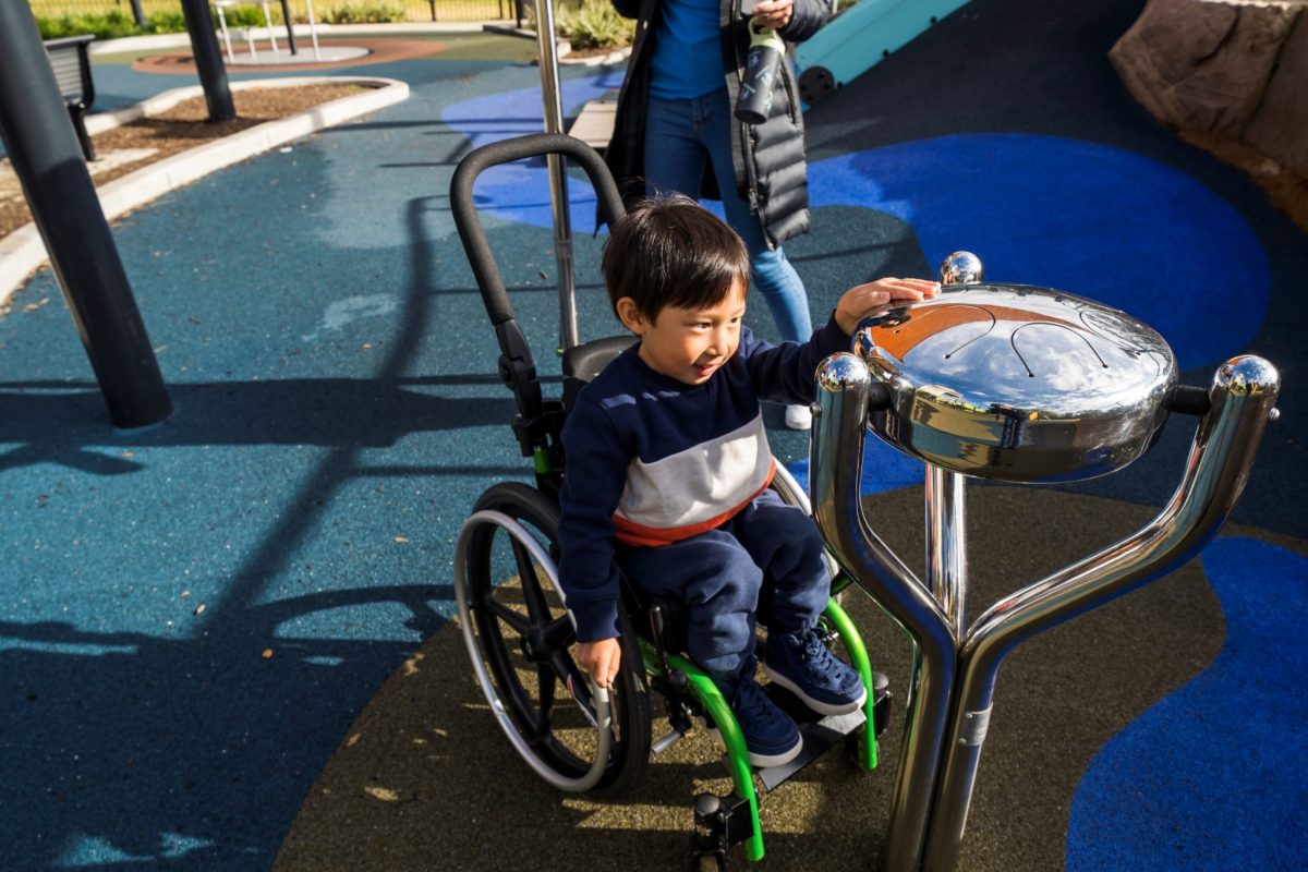 Boy in wheelchair playing a musical instrument at playground